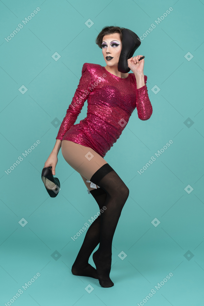 Ritratto di una drag queen con in mano una scarpa con tacco alto vicino all'orecchio