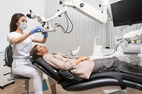 Pleine longueur d'une femme dentiste examinant sa patiente et regardant à travers le microscope