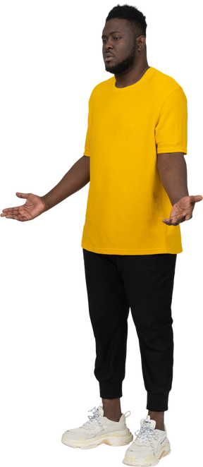 Three-quarter view of a displeased young dark-skinned man in yellow t-shirt outspreading hands