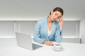Tired female office worker sitting at table with laptop