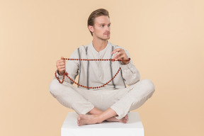 Young caucasian man sitting in lotus position and holding necklace