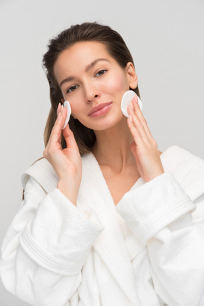 Beautiful young woman cleaning her face with cotton pad