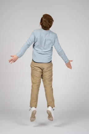 Back view of a boy in a blue shirt jumping with his arms outstretched