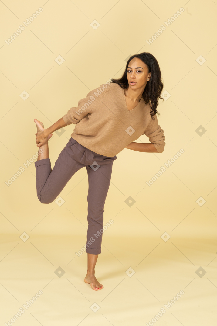 Vista frontal de uma jovem mulher de pele escura tocando seu tornozelo enquanto se inclina para frente
