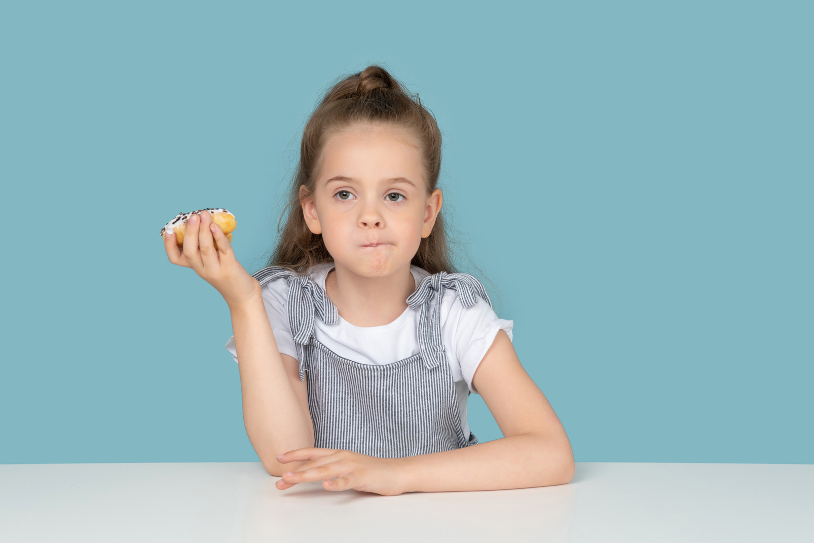 Cute little girl holding a doughnut and thinking