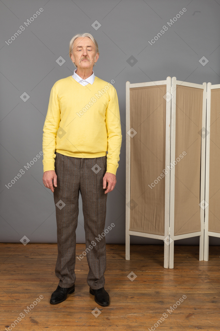 Front view of an old man standing still while looking at his nose