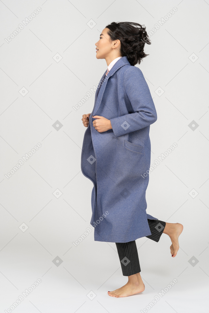 Side view of young woman in coat running