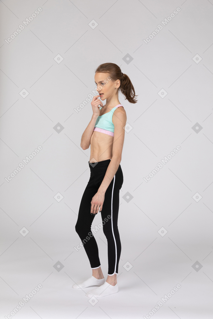Вид в три четверти задумчивой девушки-подростка в спортивной одежде, кусающей палец