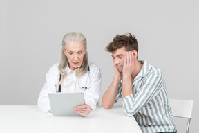 Vieille femme médecin montrant quelque chose sur sa tablette numérique à un patient