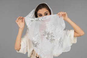 Cheerful young arab woman covering face with white shawl with silver embroidery