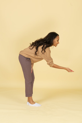 Side view of a dark-skinned young female bending down and outstretching hand