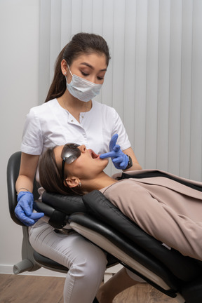 Eine zahnärztin in maske, die ihre patientin in einer medizinischen brille untersucht