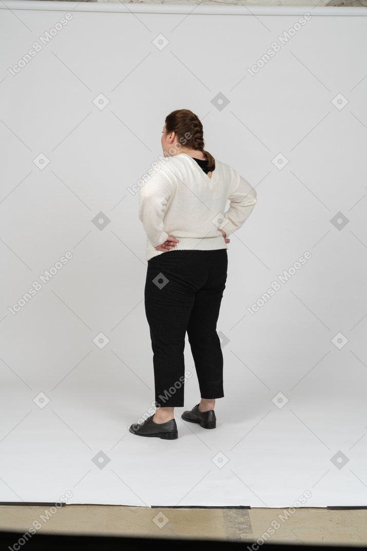 엉덩이에 손을 얹고 서 있는 평상복을 입은 통통한 여성의 뒷모습