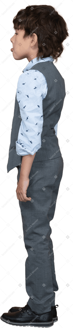 Vista lateral de um menino fofo em um terno cinza fazendo caretas