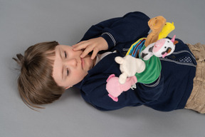 Lying little boy looking attentively at fluffy toys
