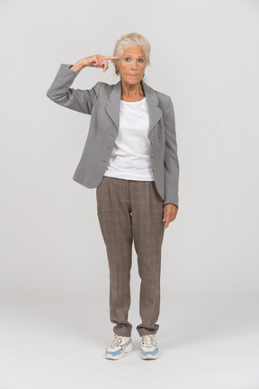Vista frontal de una anciana en traje mirando a la cámara y mostrando el signo de tornillo suelto