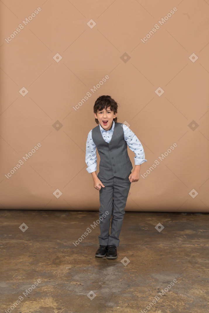握りこぶしで立ってカメラを見ているスーツを着た怒っている少年の正面図