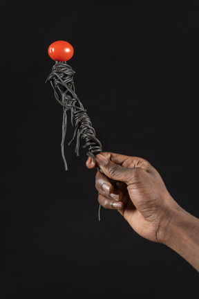 Close-up of a human hand holding black pasta with cherry tomato