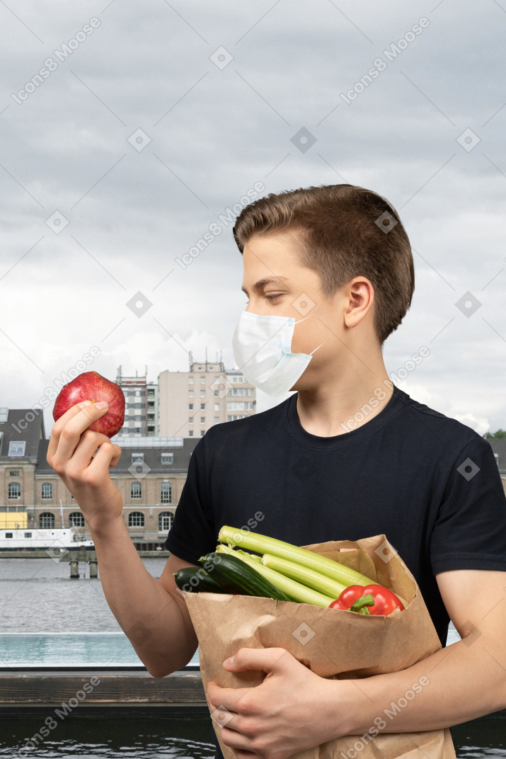 A man holding a bag of vegetables and an apple