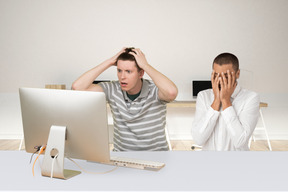 A shocked man looking at computer screen next to an upset man