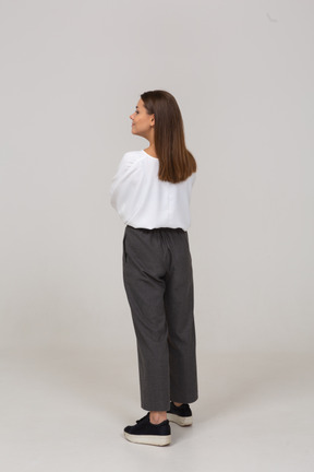 Vista posterior de tres cuartos de una joven sonriente en ropa de oficina mirando a un lado