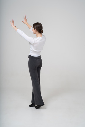 Vista lateral de uma mulher de calça preta e blusa branca em pé com os braços erguidos