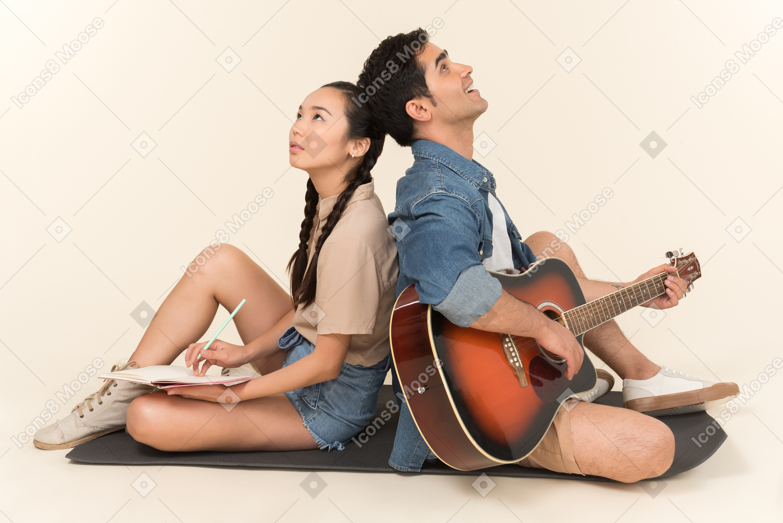 Ridere coppia interrazziale seduti schiena contro schiena e uomo a suonare la chitarra