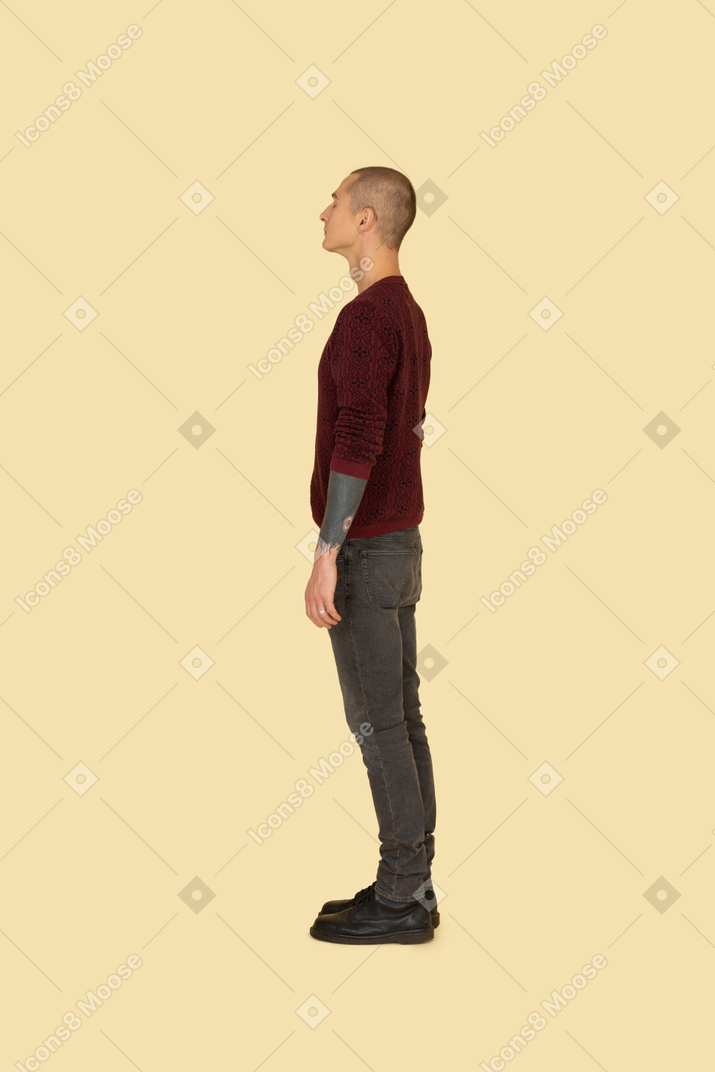 Вид сбоку на молодого человека в красном свитере, стоящего на месте