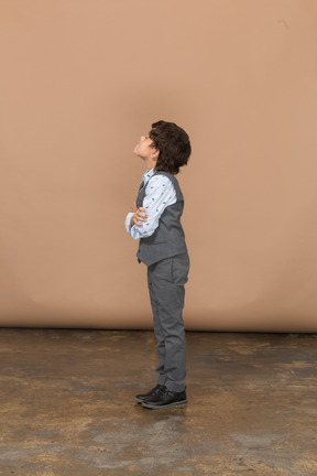 Vista lateral de un niño con traje gris abrazándose a sí mismo