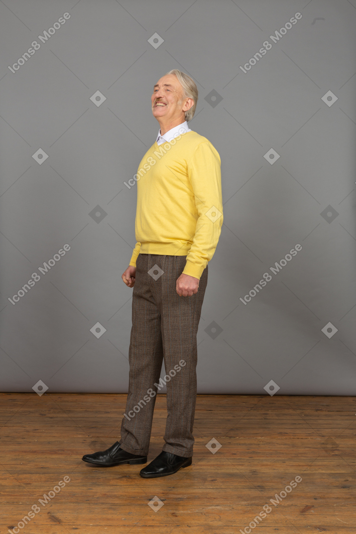 Three-quarter view of a smiling happy old man in a yellow pullover looking aside