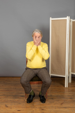 Middle-aged man sitting on chair and covering his face