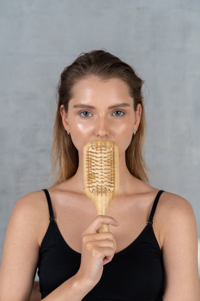 Vista frontale di una giovane donna che nasconde la bocca dietro la spazzola per capelli