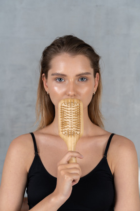 Front view of a young woman hiding mouth behind hairbrush