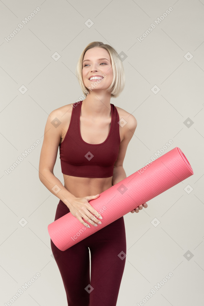 ヨガのマットを保持しているスポーツウェアで笑顔の若い女性