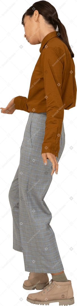 Vista laterale di una giovane donna asiatica in calzoni e camicetta che fa una riverenza