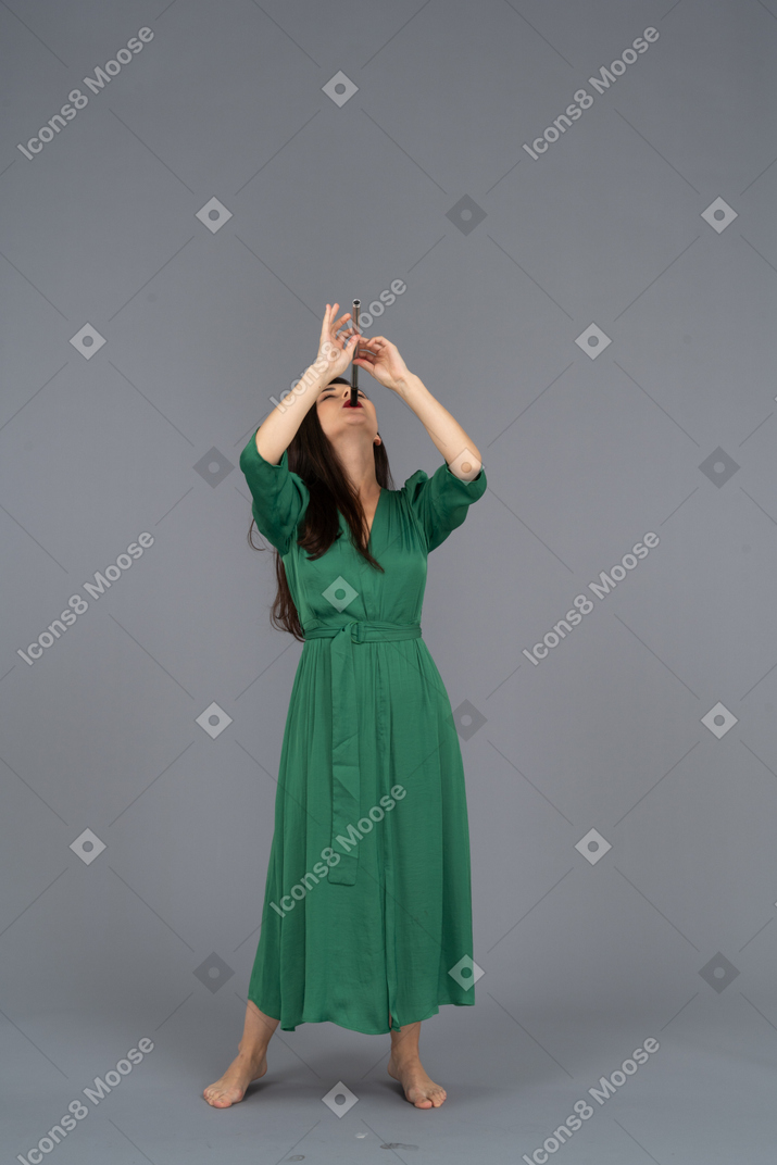 Vista frontal de una joven en vestido verde tocando la flauta mientras se inclina hacia atrás