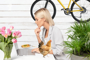 A woman sitting at a table with a laptop and a chicken