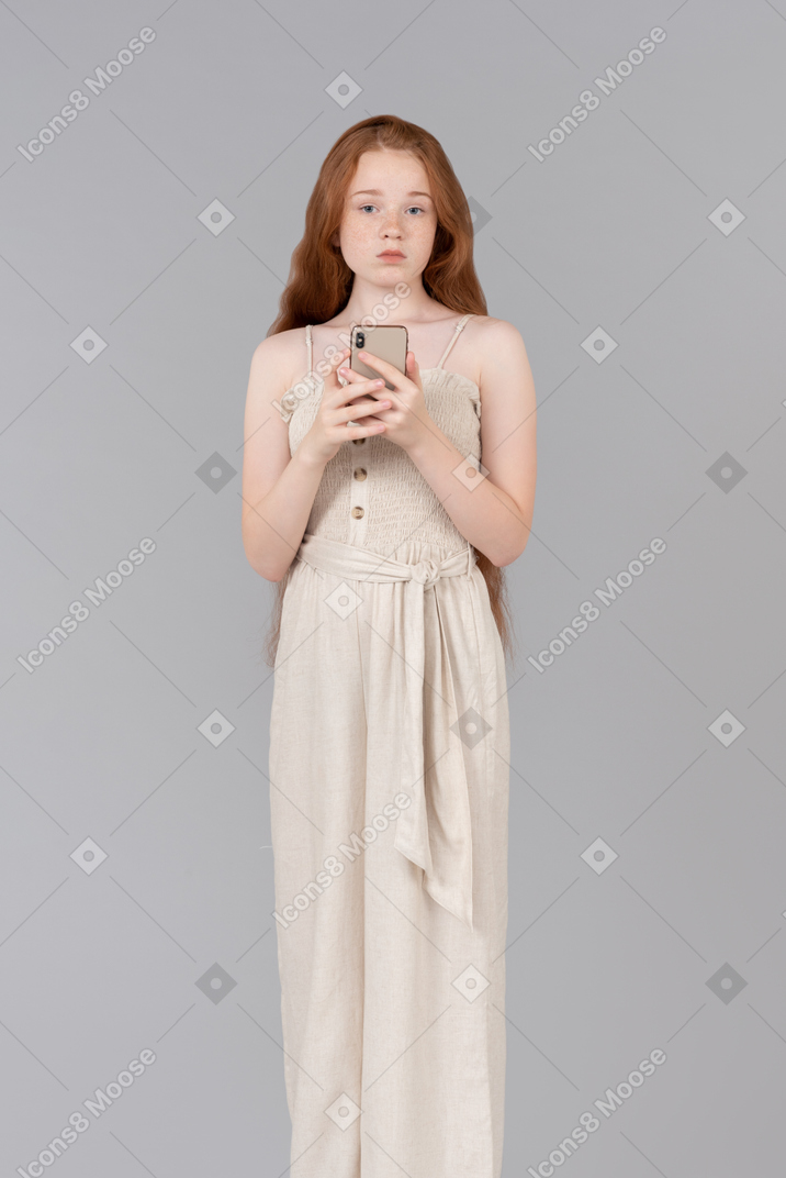 Pensive teenage girl holding smartphone and looking aside