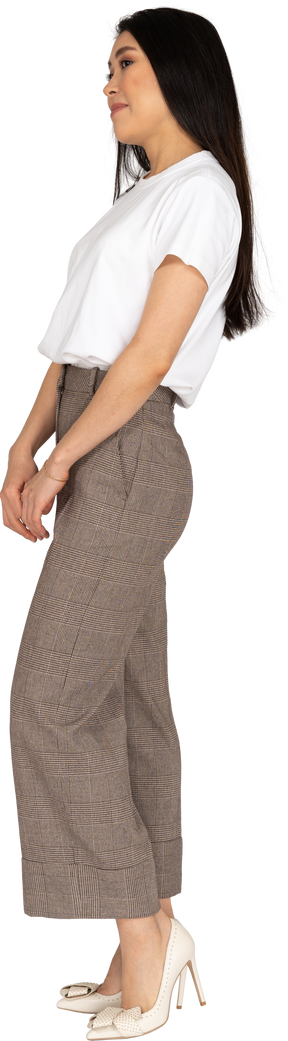 Vista laterale di una giovane donna confusa in calzoni e maglietta che tengono le mani insieme