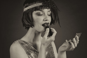 Flapper glamorosa aplicando un lápiz labial y mirando el espejo de mano