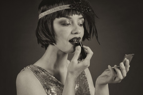 Glamorous flapper applying a lipstick and looking at hand mirror