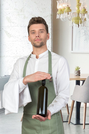 A man in an apron holding a bottle of wine