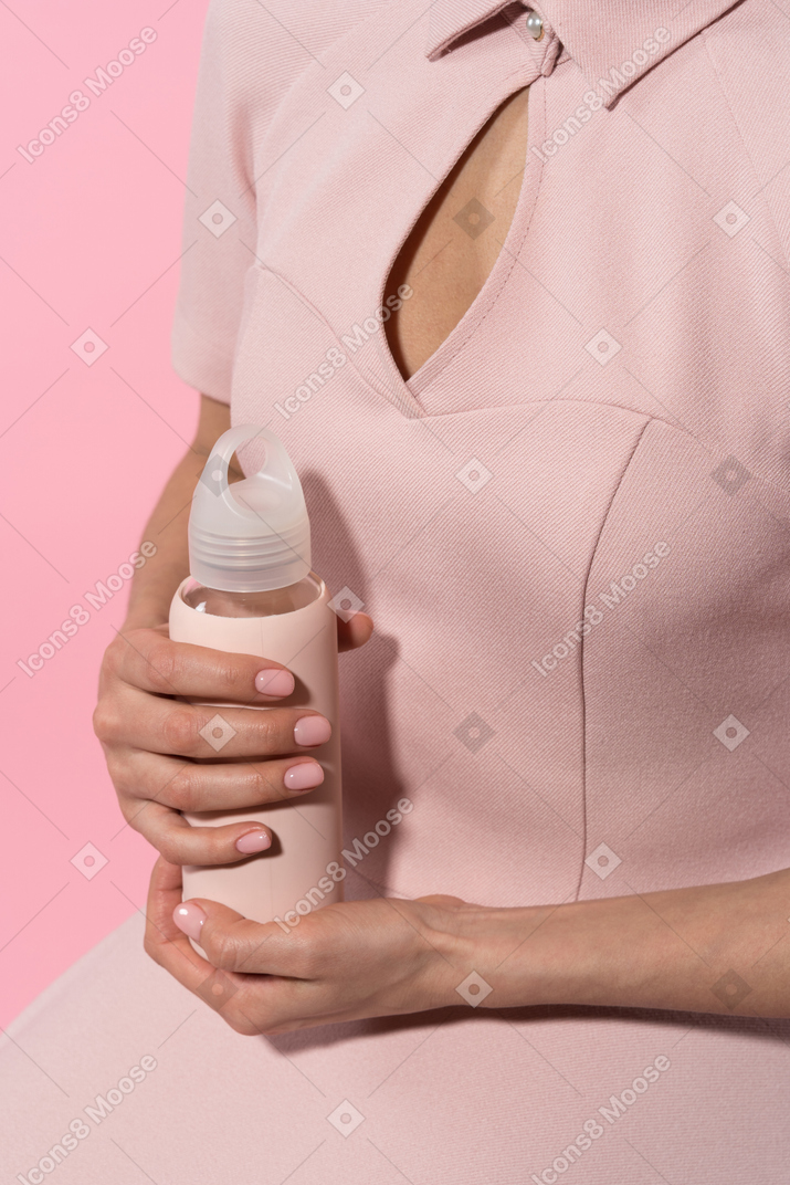Держит розовую бутылку с водой