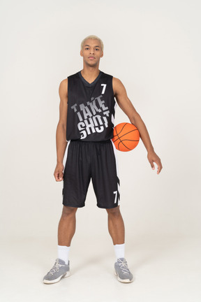Вид спереди молодого баскетболиста мужского пола, держащего мяч