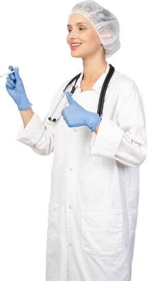 Vista de tres cuartos de una sonriente joven doctora con estetoscopio sosteniendo el termómetro y mostrando el pulgar hacia arriba