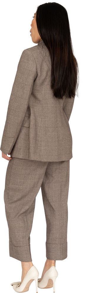 Three-quarter back view of a surprised young lady in brown business suit
