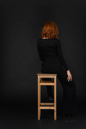 A back side view of the cute girl sitting on the chair in the dark room