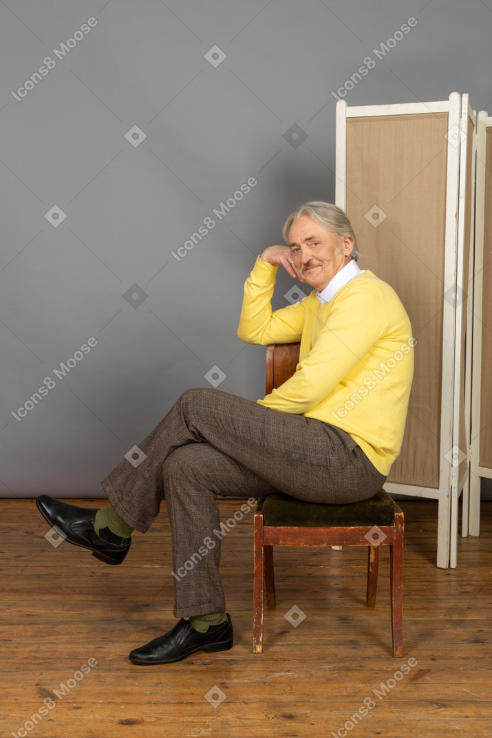 Vue latérale d'un homme assis sur une chaise et regardant la caméra