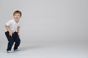 Улыбающийся маленький мальчик стоит с согнутыми коленями
