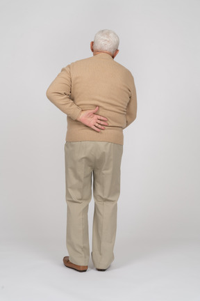 背中の痛みに苦しんでいるカジュアルな服を着た老人の背面図